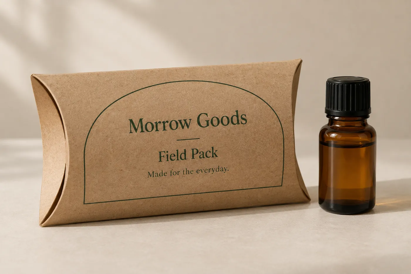 Closed kraft pillow box with curved ends, forest-green print, and an amber fragrance bottle