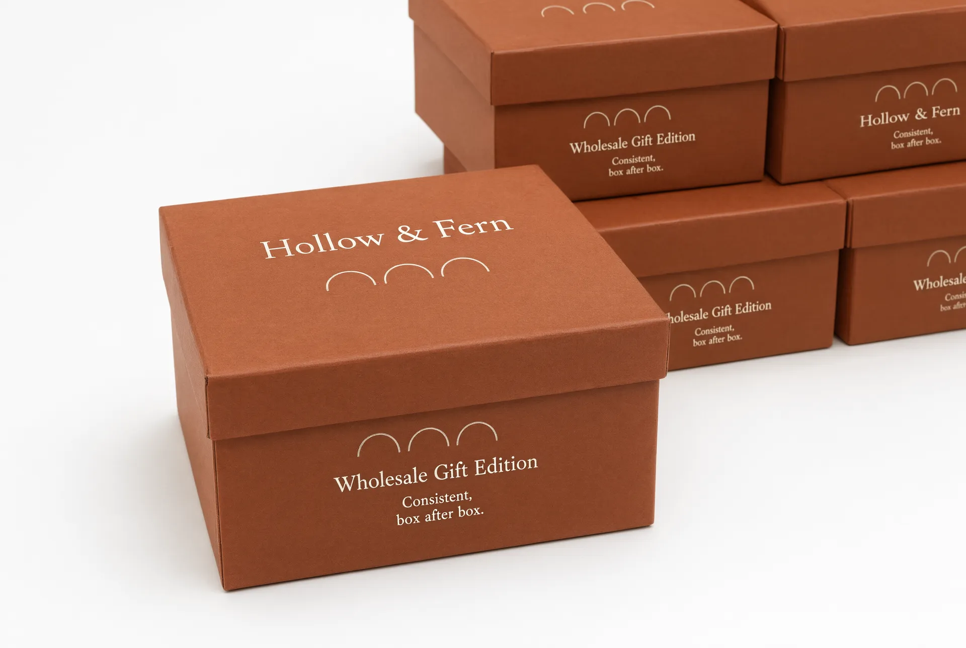 Closed terracotta gift box with ivory foil motif, stacked in front of several matching closed boxes